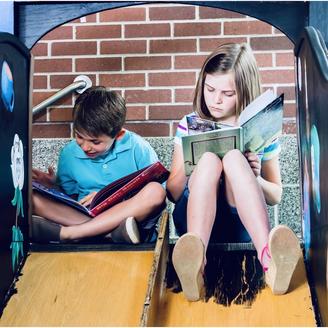 Deux enfants (un garçon et une fille) lisent au sommet d'une glissoire.