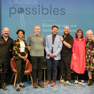 Sept personnes debout devant un écran sur lequel est écrit : « L'audace des possibles. Ensemble vers une société apprenante. »